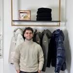Man wearing a turtleneck standing by winter jackets on display.