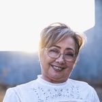 Portrait of a smiling senior woman wearing glasses and a white blouse in natural sunlight.